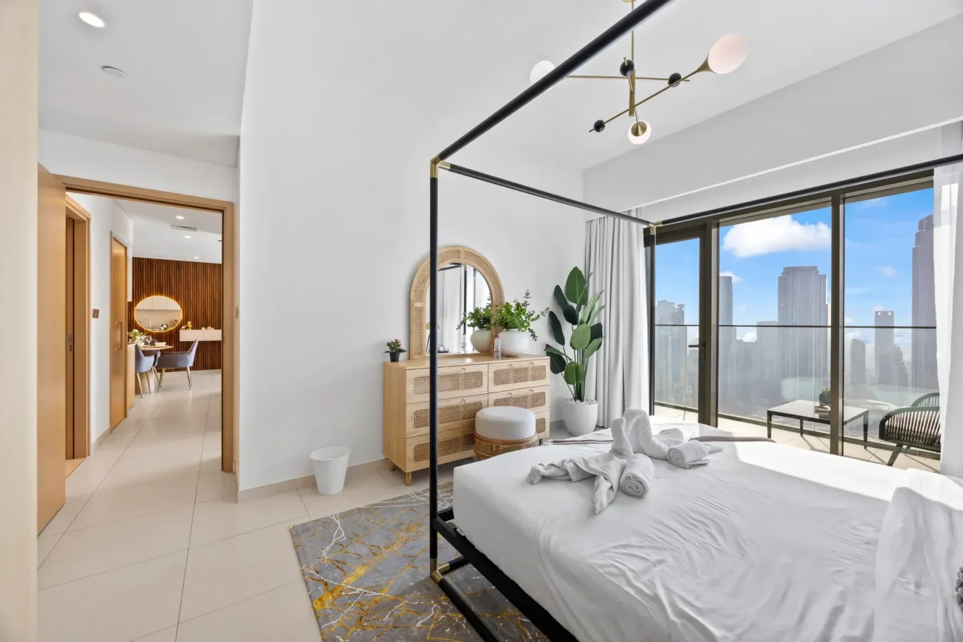 Bedroom with a black metal canopy bed, white linens, and a view of a city skyline through large glass doors.