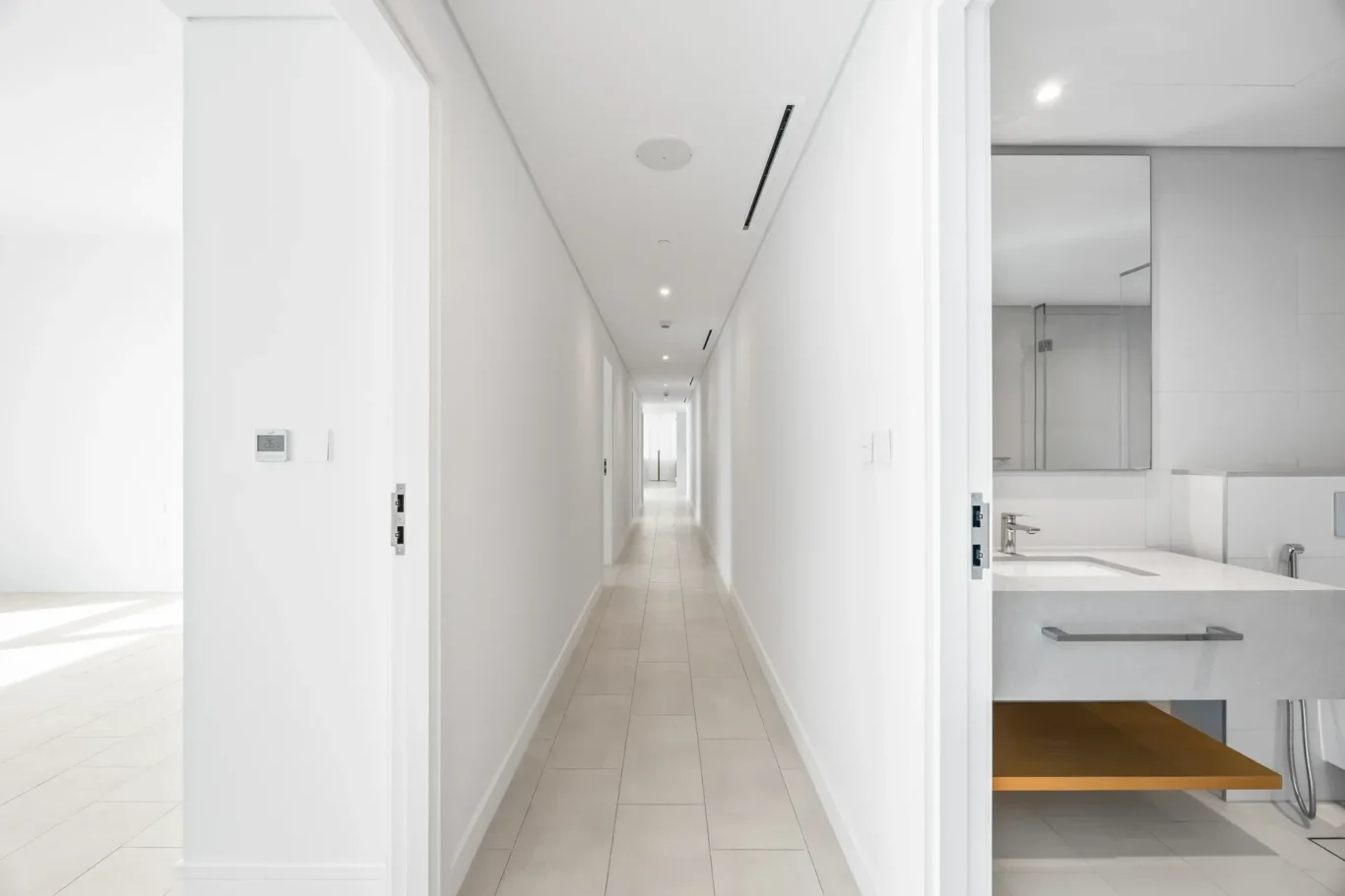 Bright white, minimalist hallway with doors along both sides and a modern bathroom visible on the right side.