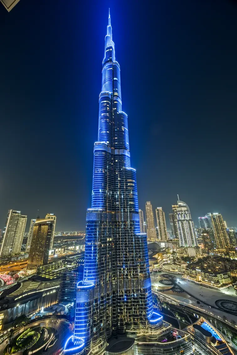 Burj Khalifa illuminated in blue at night, towering above Dubai skyline.