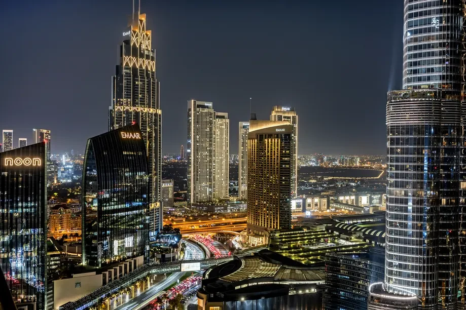 Nighttime city skyline with tall illuminated skyscrapers and a network of lit roads.