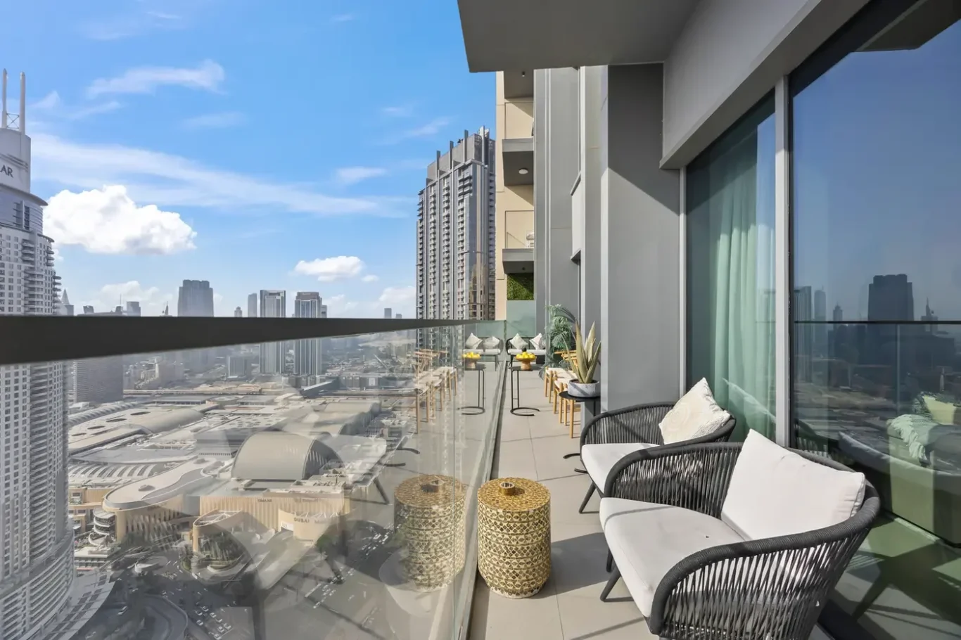 Balcony seating area with wicker chairs and cushions, overlooking a city skyline of tall buildings and a clear blue sky.