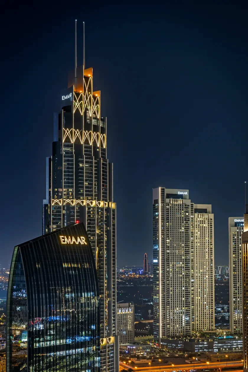 Night view of Dubai skyline at dusk with illuminated EMAAR towers and glass skyscrapers bringing geometric gold accents to the scene