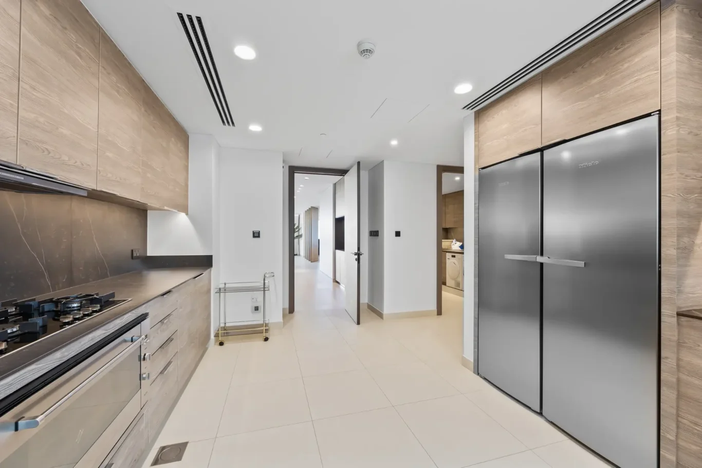 Modern kitchen with light wood cabinets, marble backsplash, gas cooktop, and a tall stainless steel refrigerator.