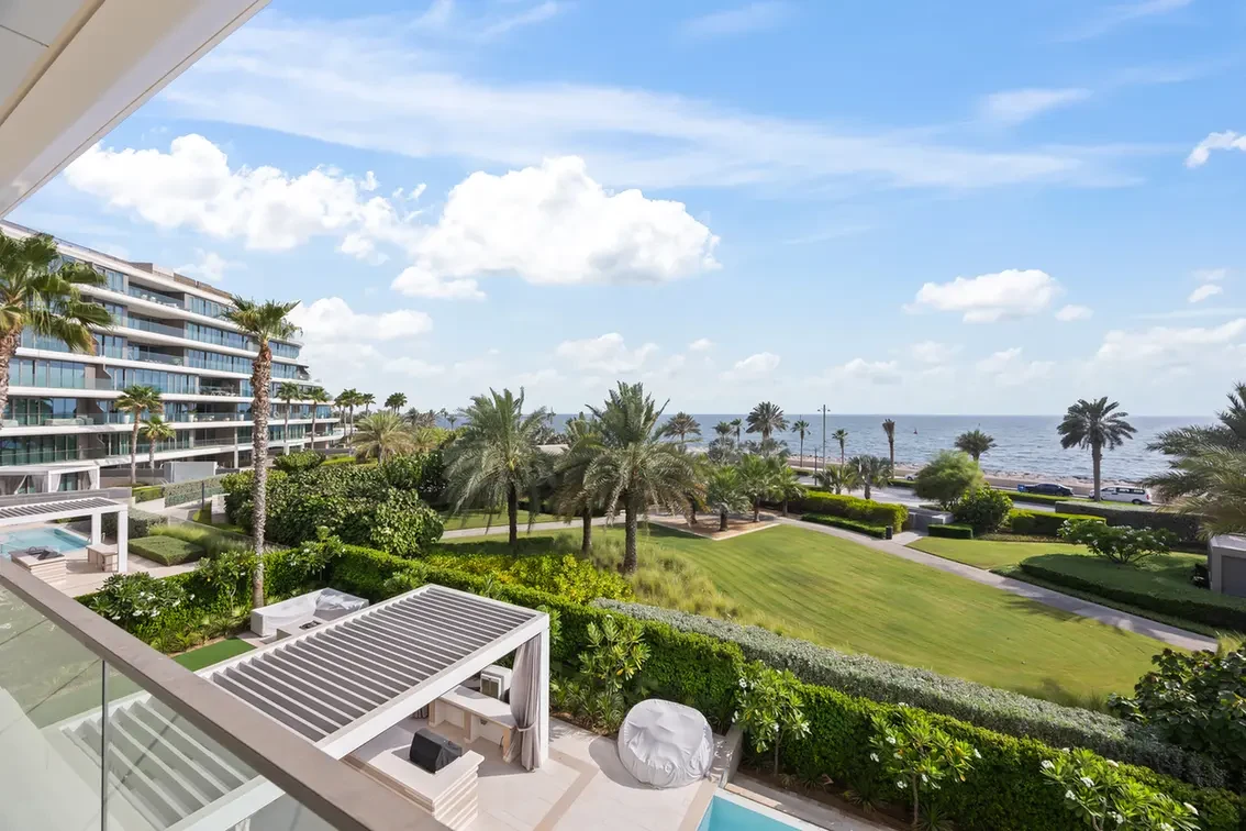 Oceanfront resort with a lawn, palm trees, and a modern apartment building, sea in the background.