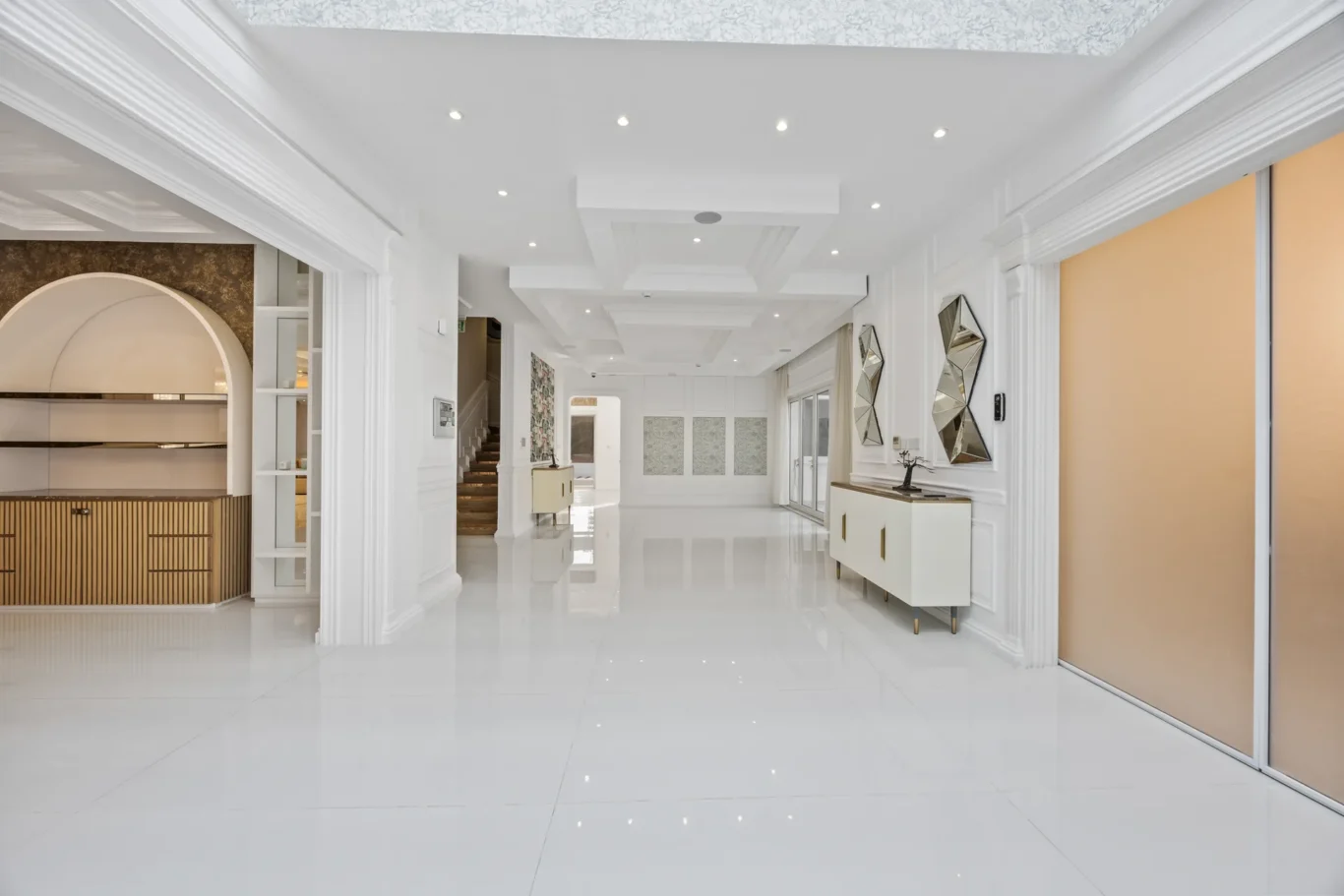 Bright white modern foyer with glossy tile floor, built-in cabinets, and abstract mirrored walls in a spacious entrance area.