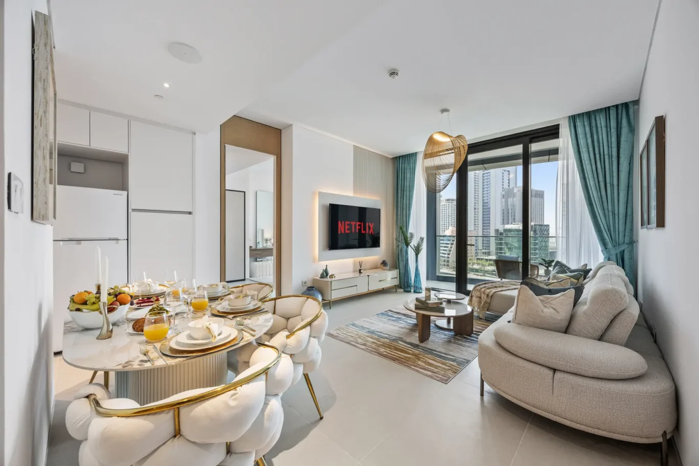 Open-plan living and dining space with a wall-mounted Netflix screen, cream sofa, and a glass dining table facing a city-view balcony.