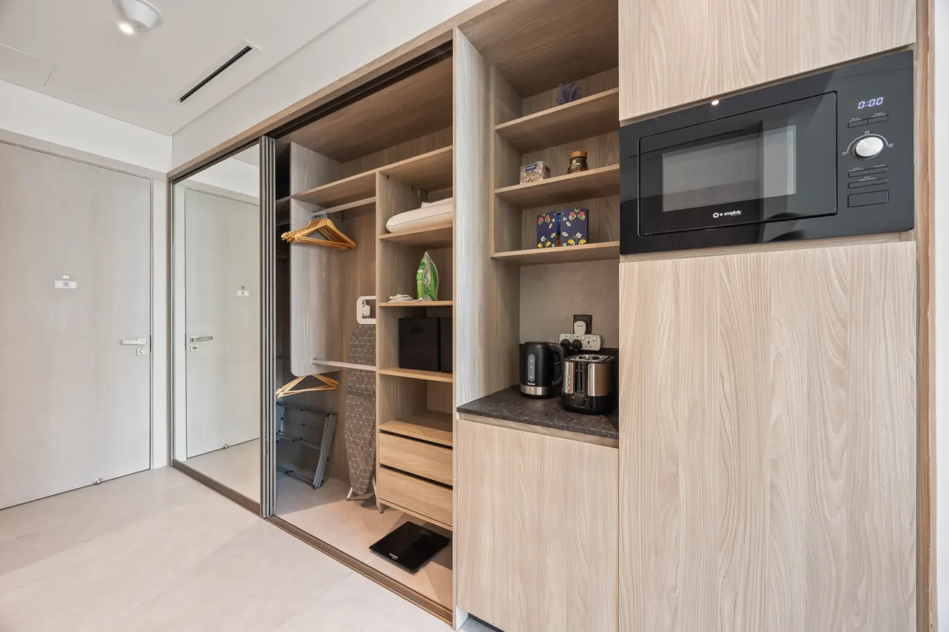 Open built-in wardrobe with hanging rail, shelves, and integrated appliances in a modern closet system.