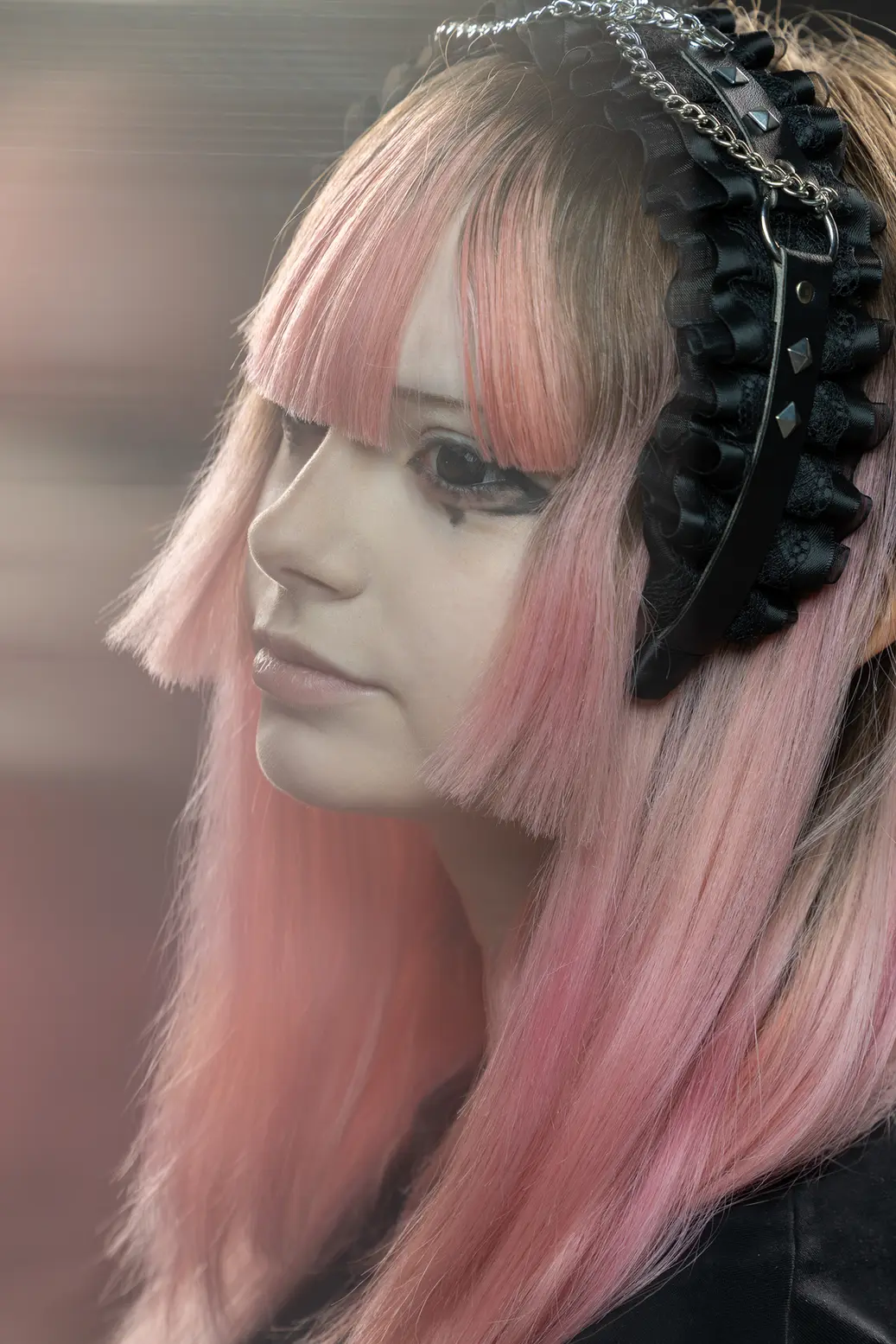 Side-profile portrait of a person with pink hair and a Gothic black ruffled headband with chains.