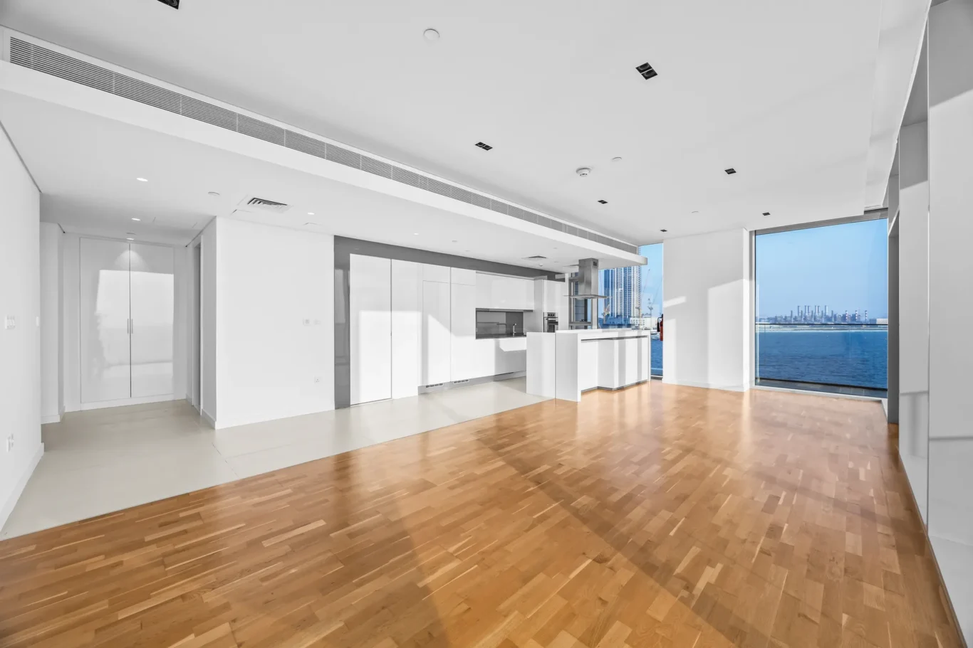 Open-concept modern kitchen with white cabinets, island, and a large window showing water and city skyline outside.