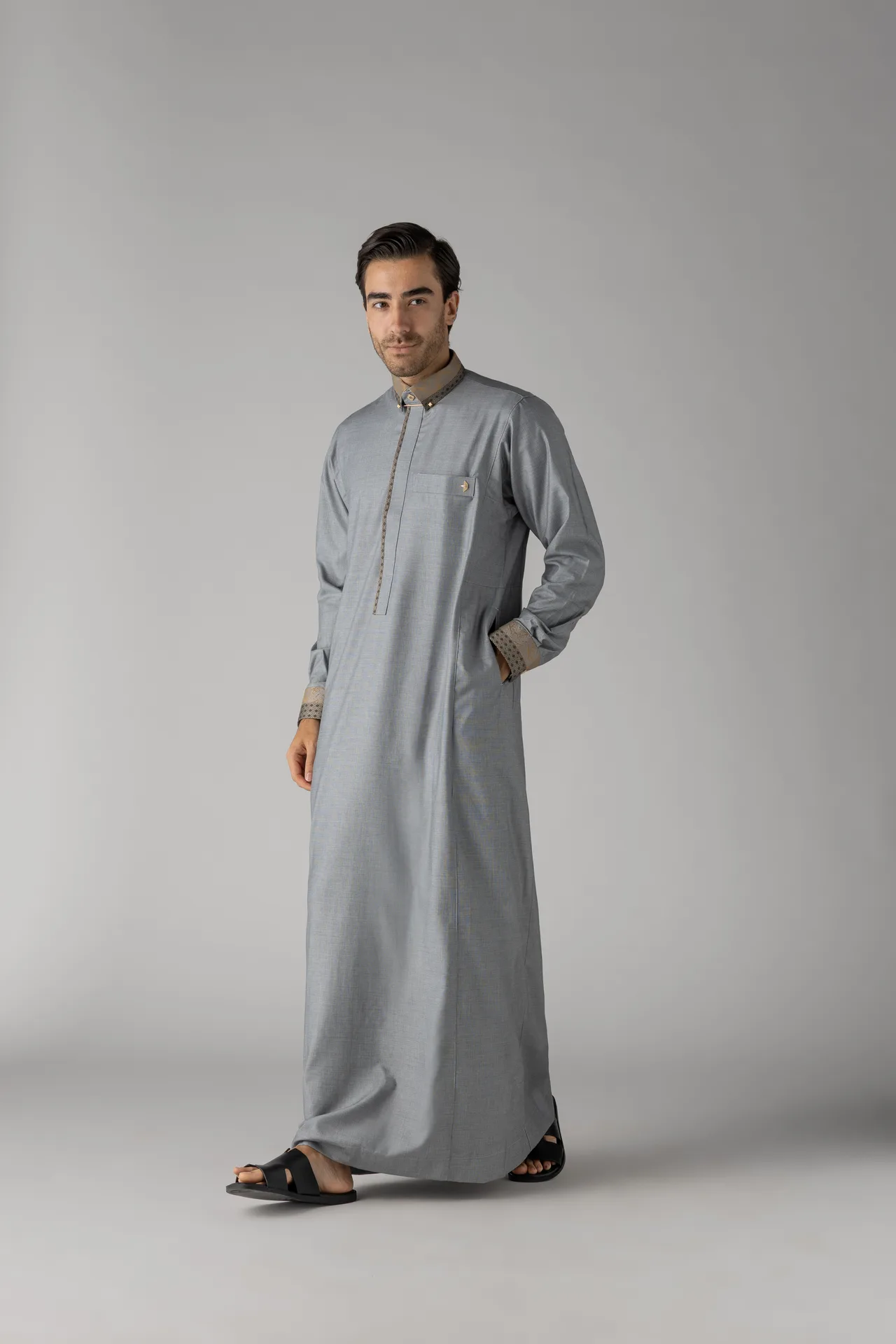 Man wearing a light gray traditional kurta with patterned cuffs and collar, standing against a plain gray background.