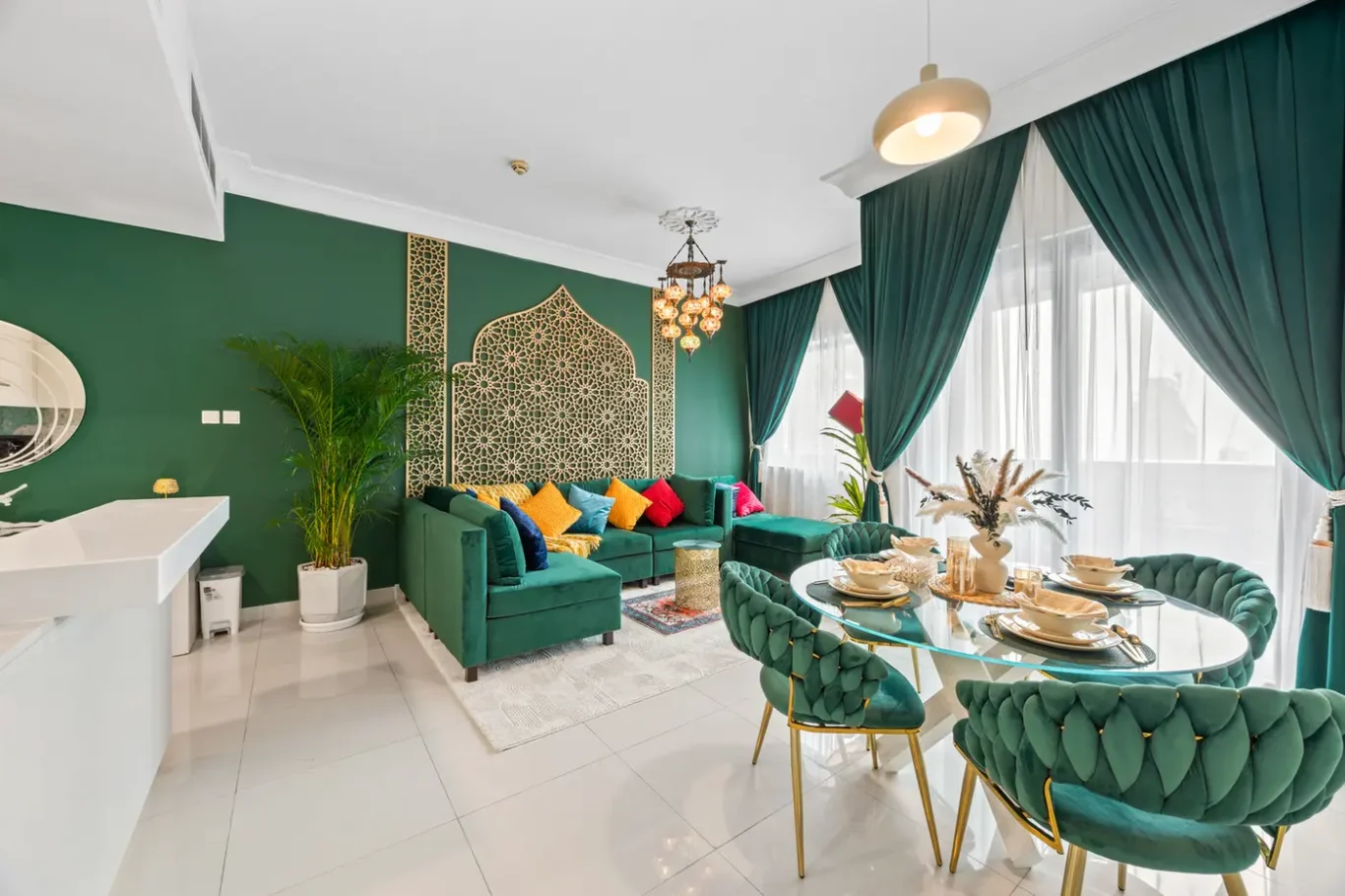 Open-plan living-dining area with emerald walls, gold lattice screen, and green velvet sofa with colorful pillows.