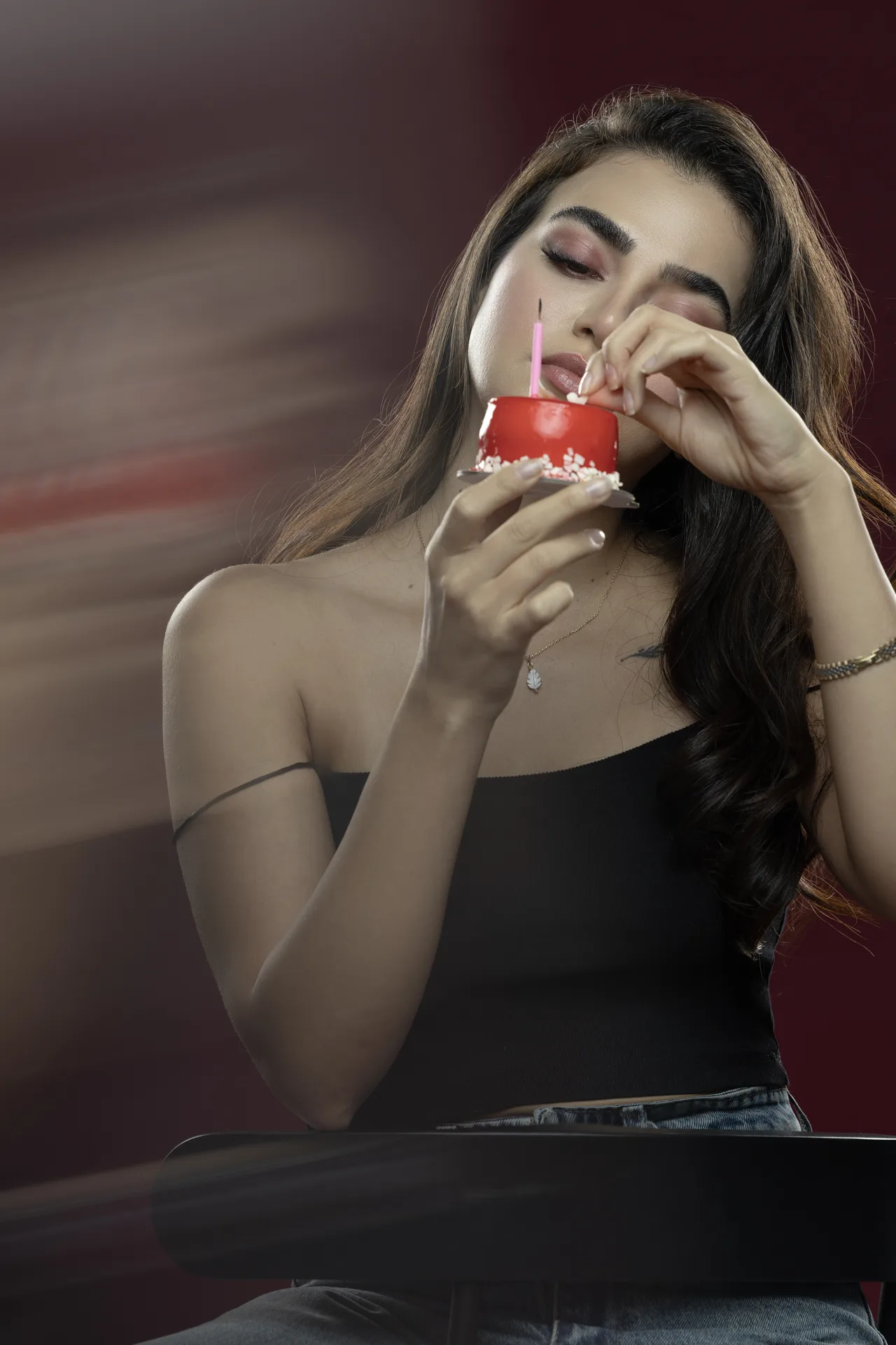 Woman holding a small red cake with a pink candle near her lips, about to blow it out