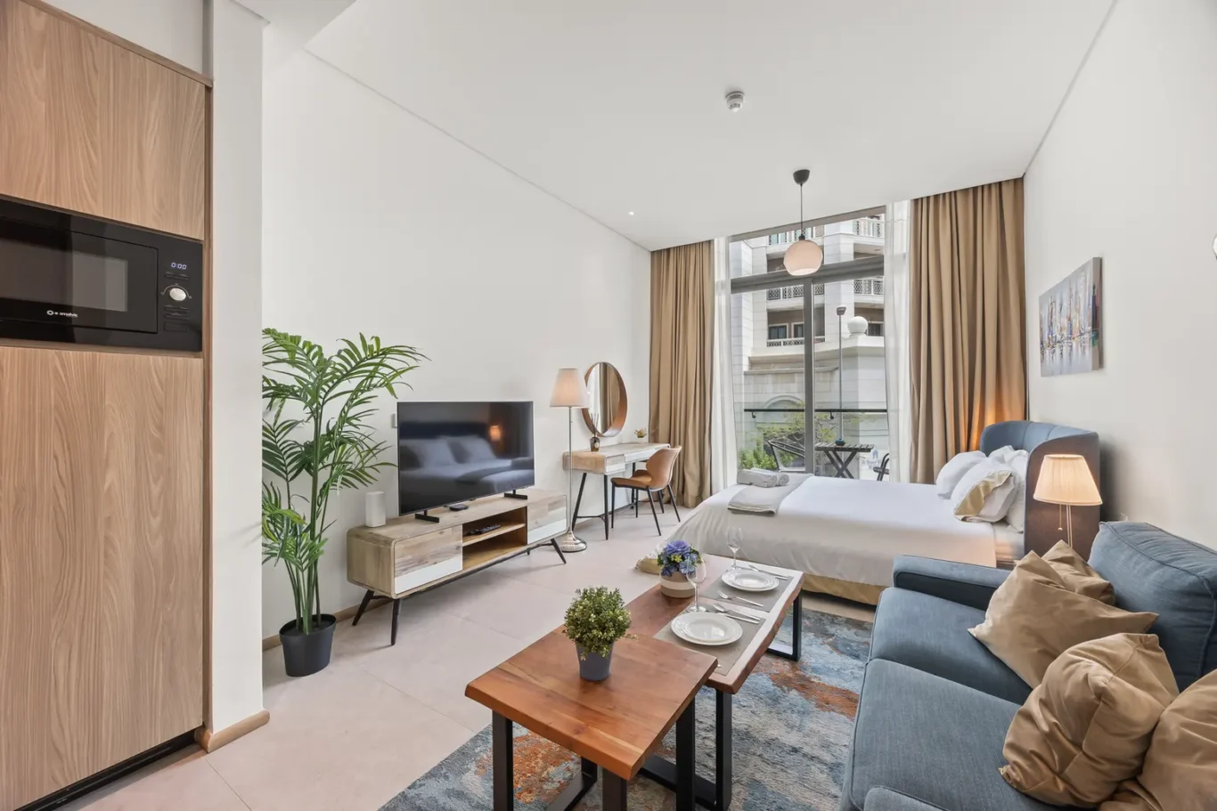 Bright hotel suite with a bed, blue sofa, and a balcony opening to city views.
