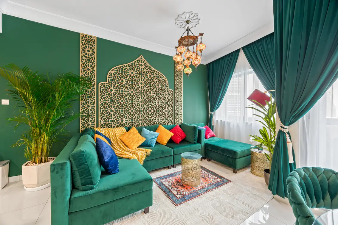 Luxurious living room with emerald walls, a green velvet sectional, and colorful cushions under a Moroccan lattice headboard design on the wall