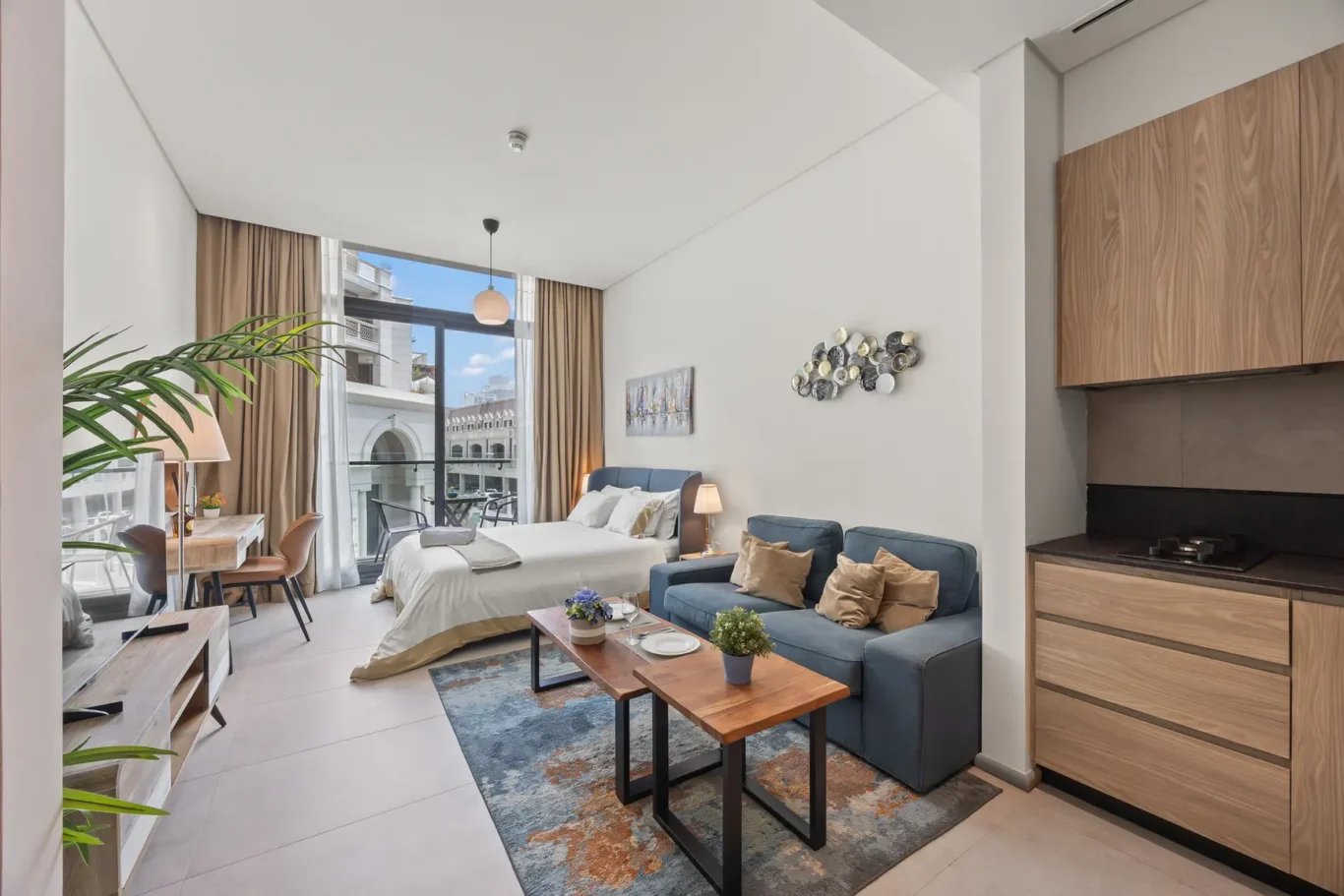 Modern hotel suite: living area with blue sofa, coffee tables, and a bed near a balcony with city view