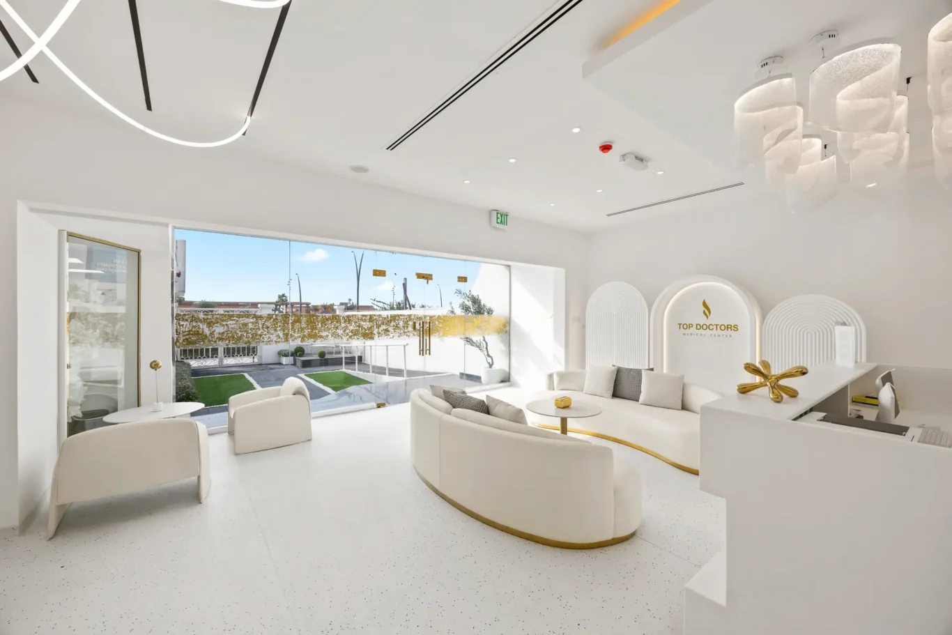 Modern white medical lobby with curved white seating, gold accents, and a 'Top Doctors Medical Center' sign on a rounded wall behind the reception desk.