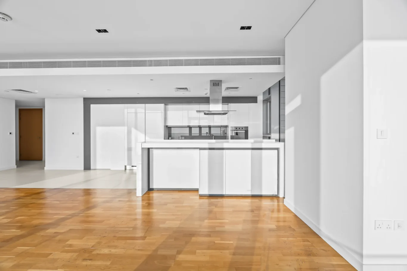 Open-plan kitchen with white cabinets, stainless steel range hood, and an island on warm wooden floors.
