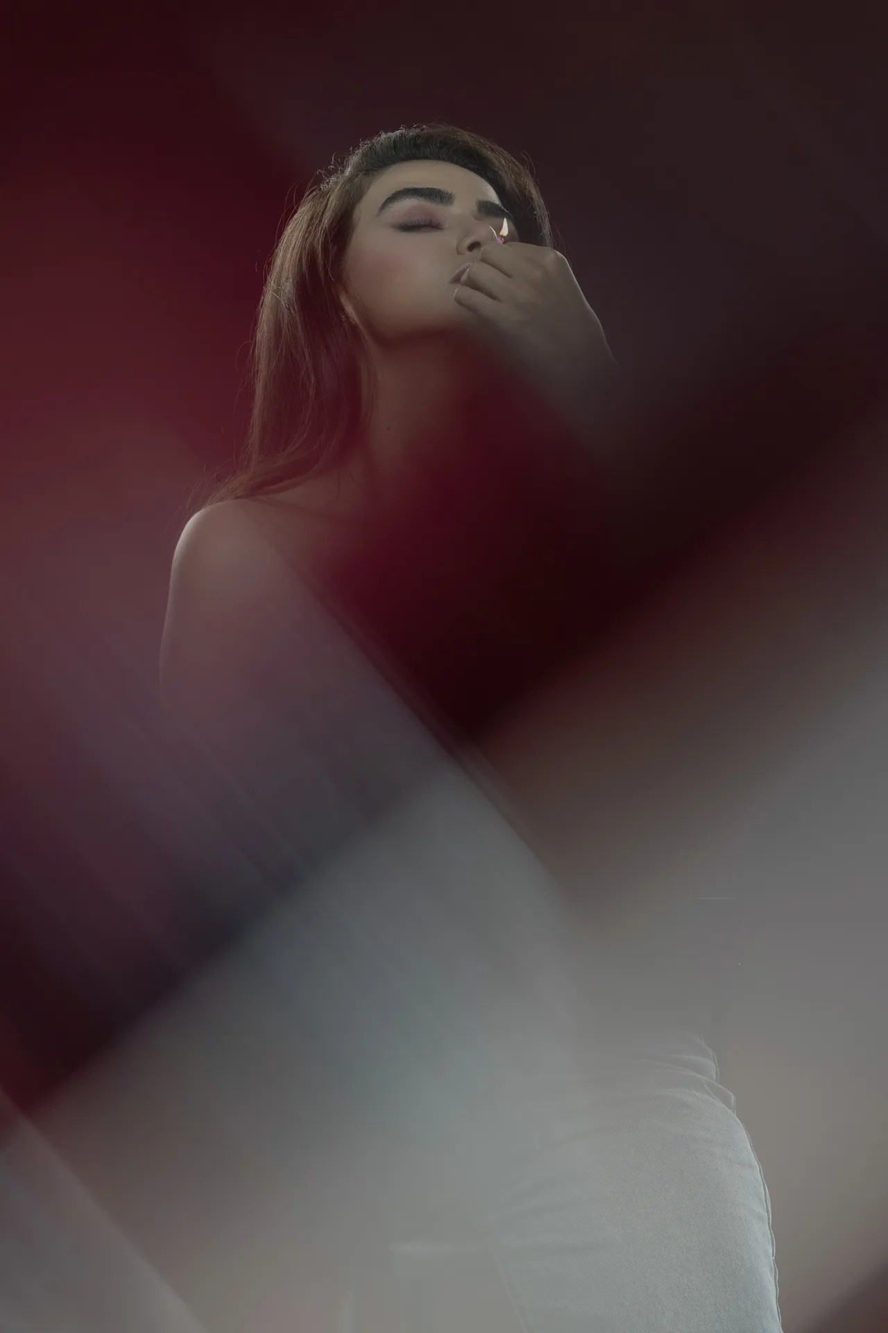 Woman with eyes closed, gently touching her lips with a finger in a moody red-lit portrait.