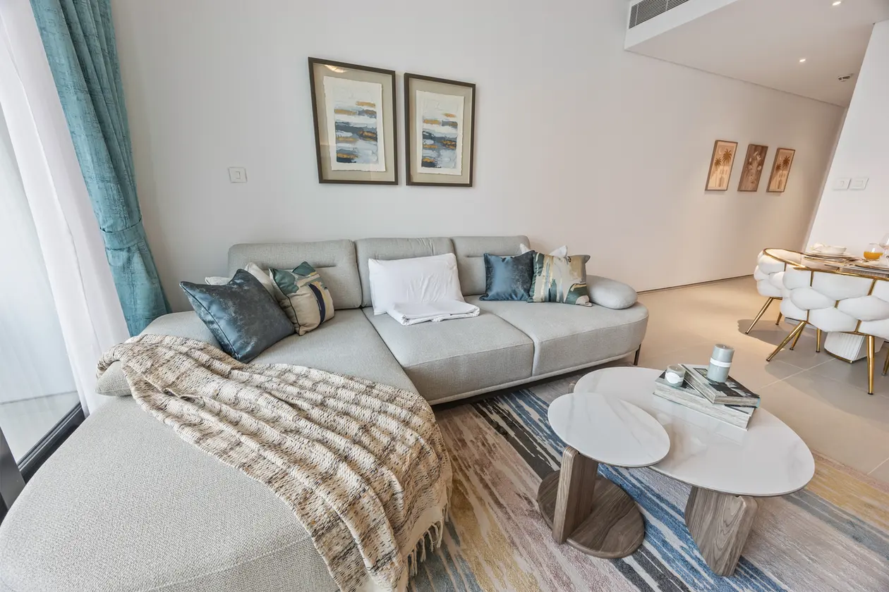 Modern living room with a light gray sectional, blue and teal pillows, and a beige textured throw blanket.
