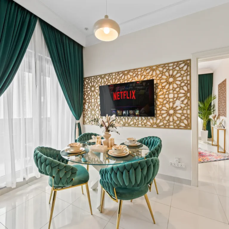 Elegant dining nook: teal velvet chairs around a round glass table, green drapes, and a Netflix screen mounted on a decorative lattice wall.