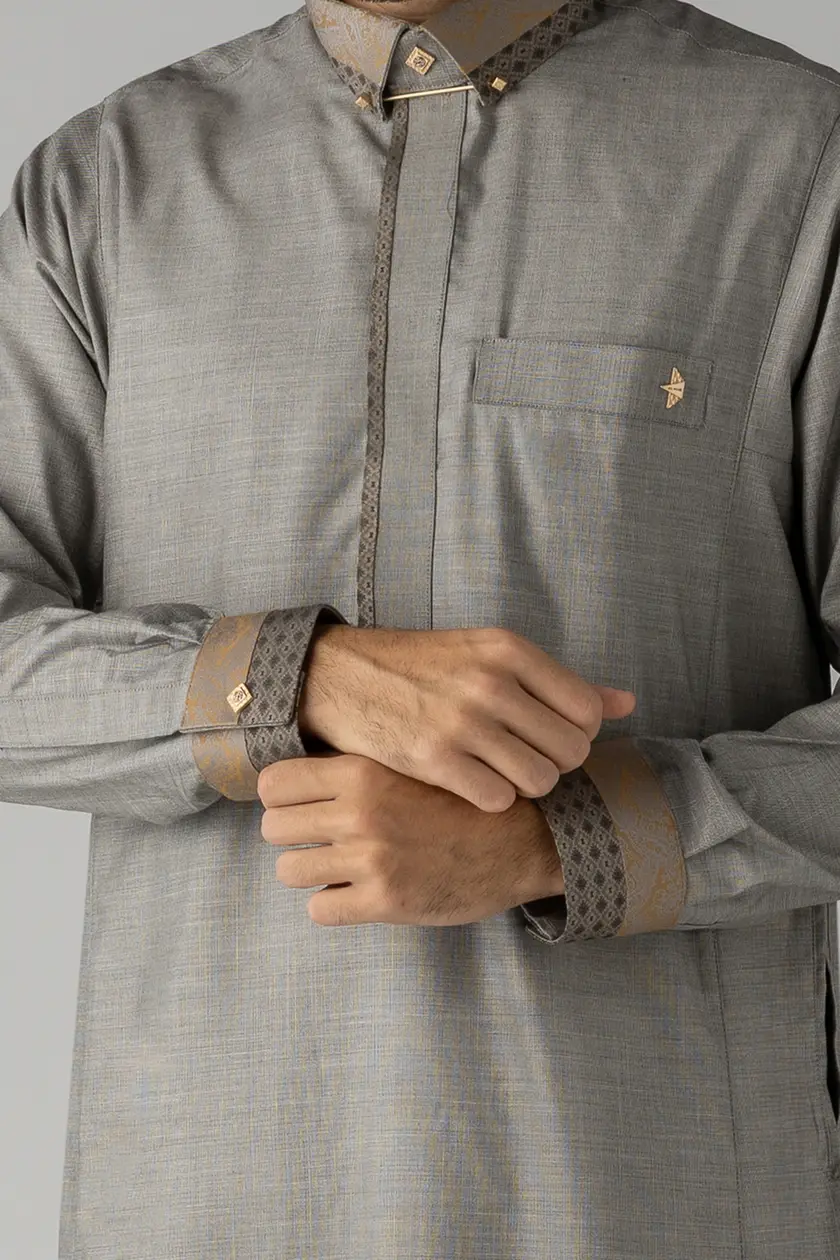 Man wearing a light gray traditional thobe with gold patterned trim along the cuffs, collar, and placket.