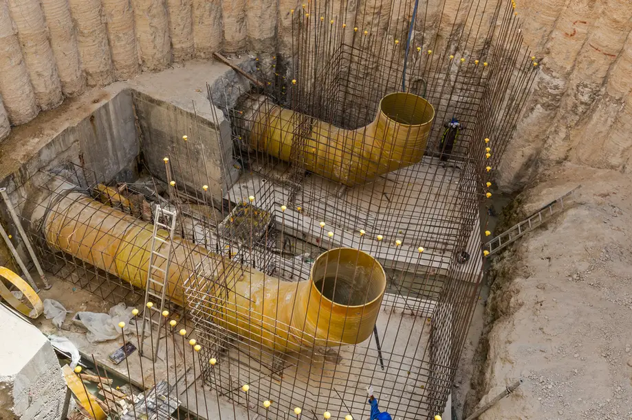 Underground construction site with yellow curved ventilation ducts and exposed rebar grid around a concrete pit.