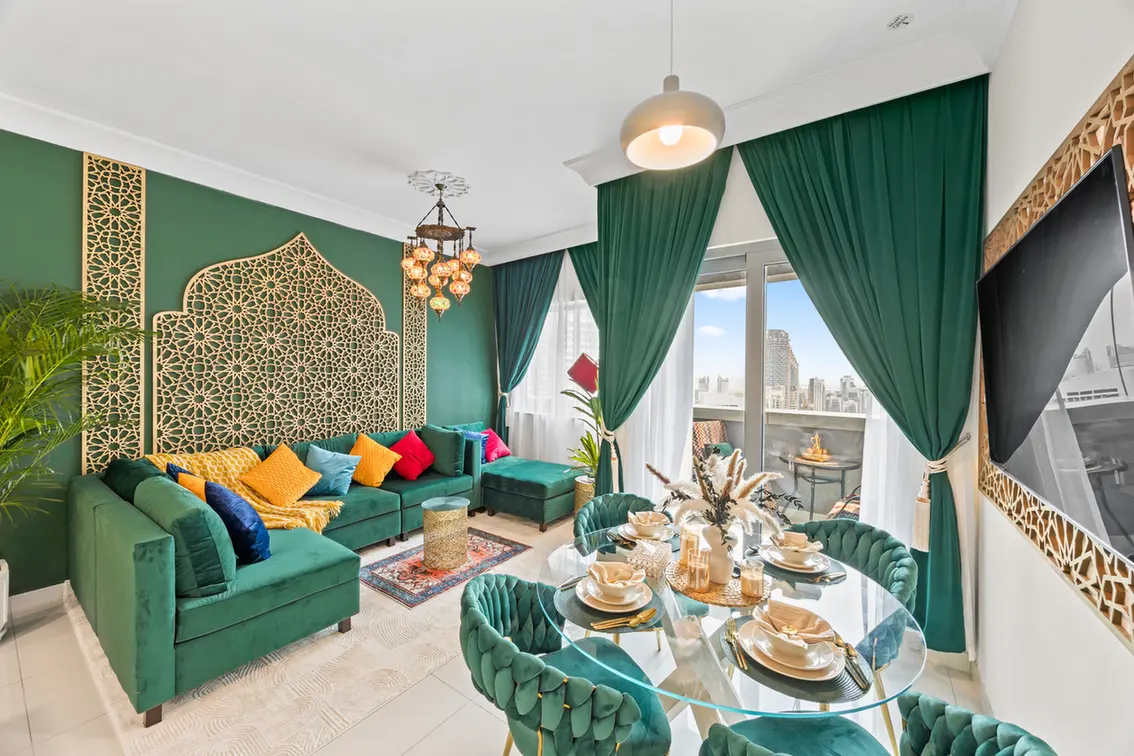 Luxurious living room with green walls, gold lattice panels, and teal sofa with colorful cushions. - Teal seating, ornate gold screens, and a glass dining table centerpiece setup in a bright room with city view.