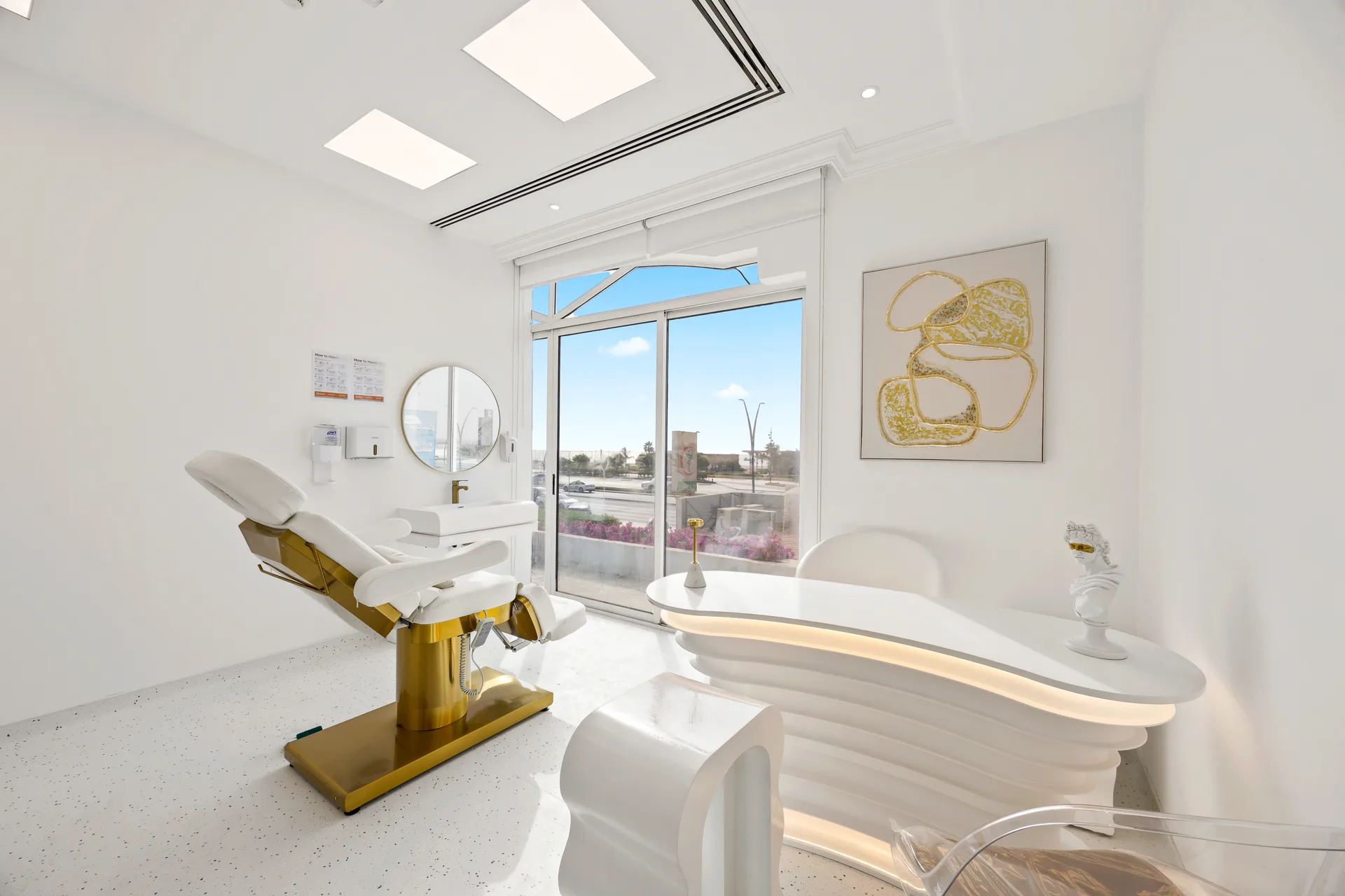 Modern dental treatment room with a white and gold reclining chair, large window, and abstract gold artwork on the wall.