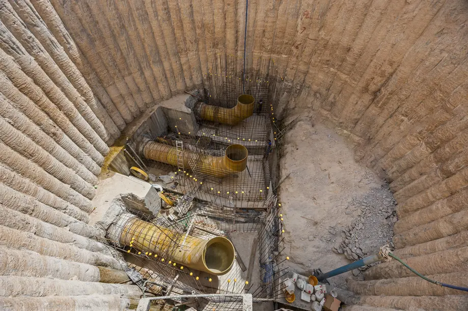 Deep excavation pit with yellow curved drainage pipes and exposed steel rebar in concentric walls.