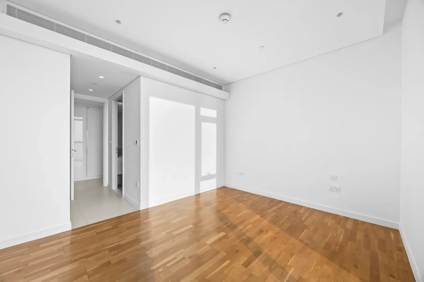 Bright, unfurnished living space with light hardwood floors and white walls, open doorway to a secondary room.