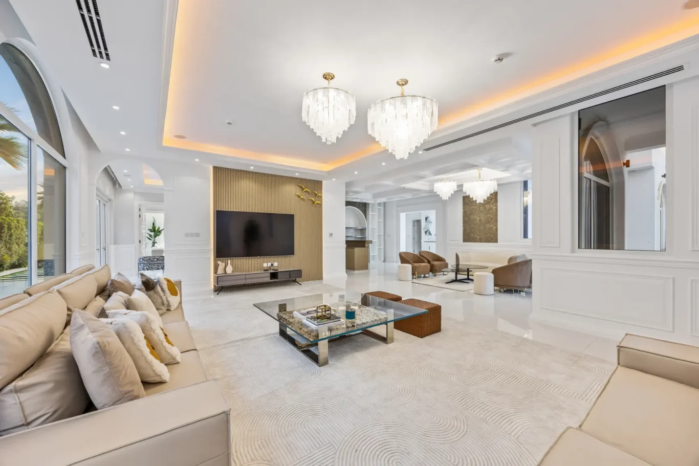 Luxurious open living room with beige sectionals, a glass coffee table, and a patterned light rug under soft lighting.