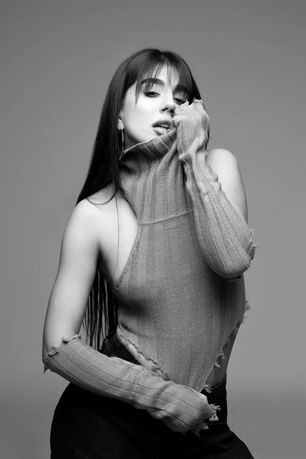 Portrait of a woman in a ribbed knit sweater pulled up over her mouth, one shoulder exposed, in grayscale.