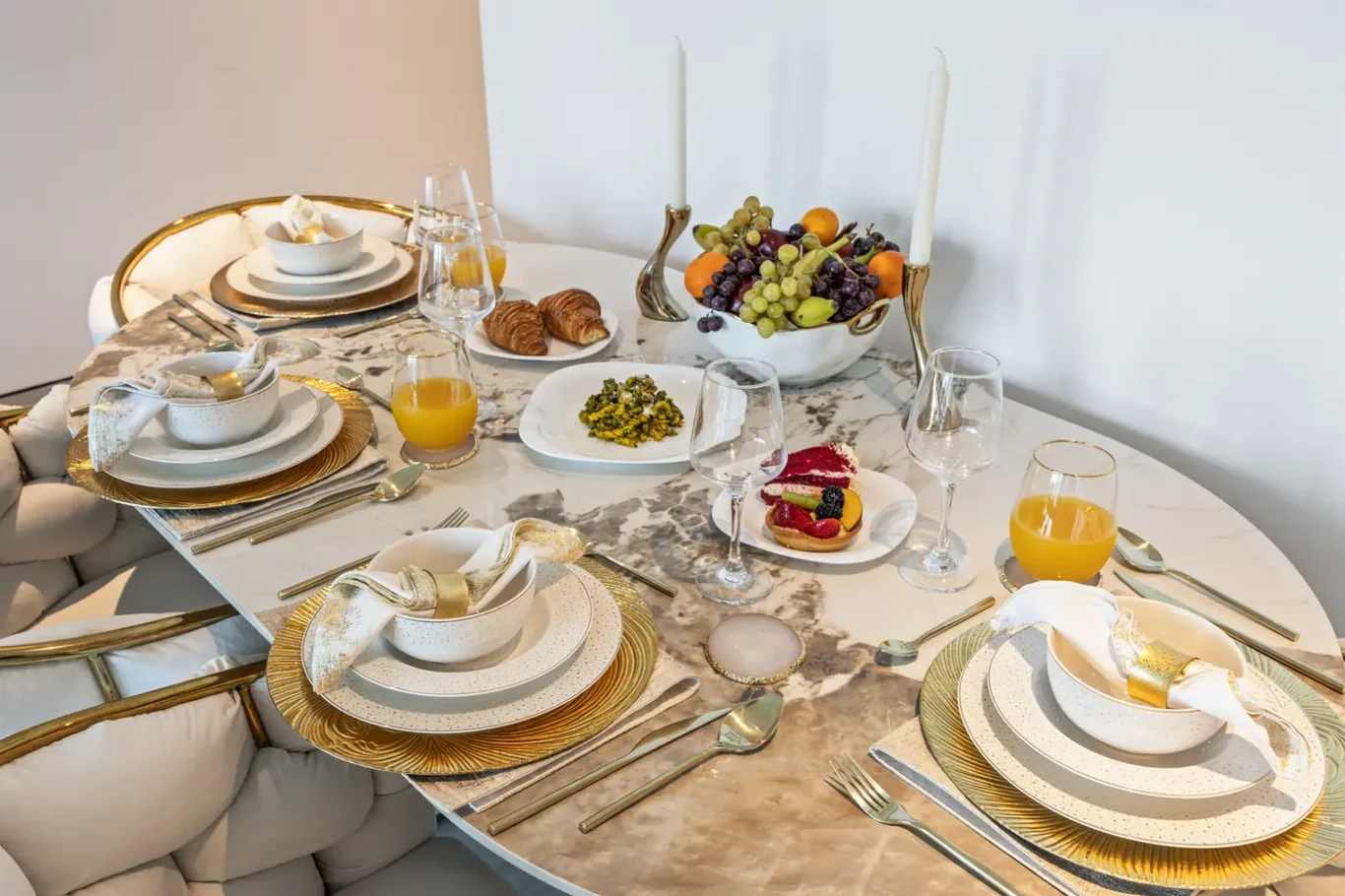 Elegant marble dining table set for a brunch with gold chargers, fine china, and a fruit centerpiece