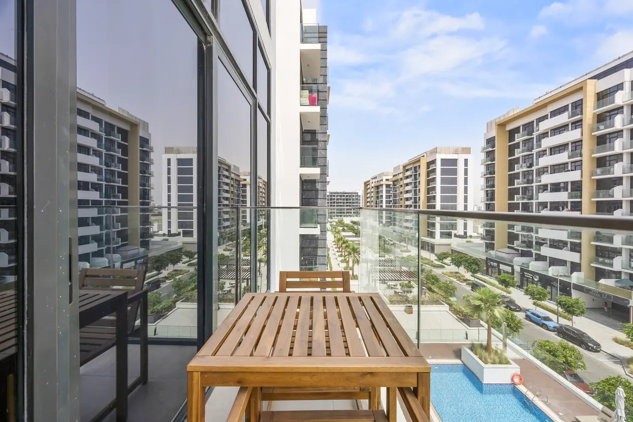 Balcony with a wooden table and chairs overlooking a modern residential complex and a pool