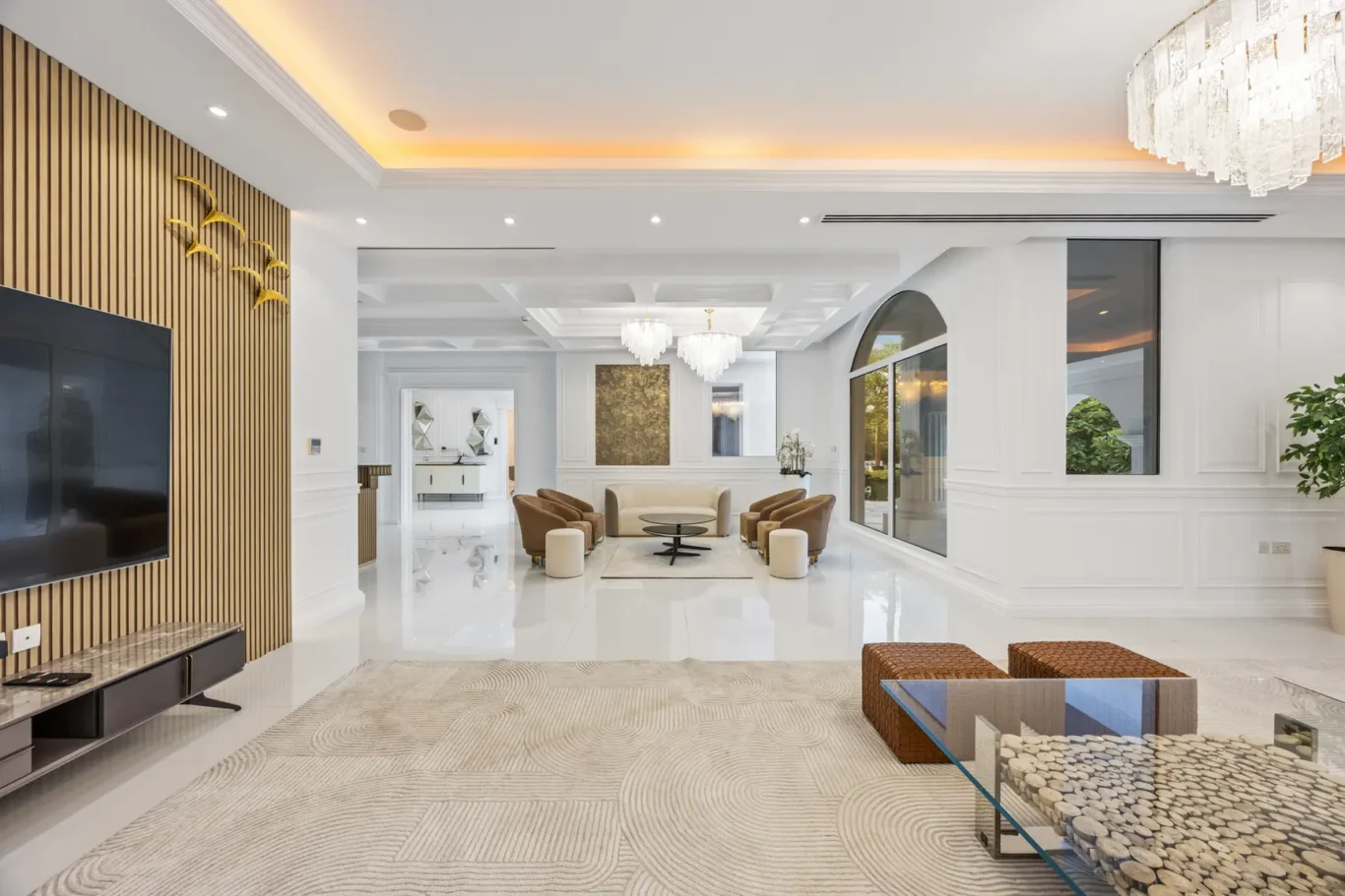Bright, modern living room with white walls, beige sofa, brown accent chairs, and a crystal chandelier centerpiece.