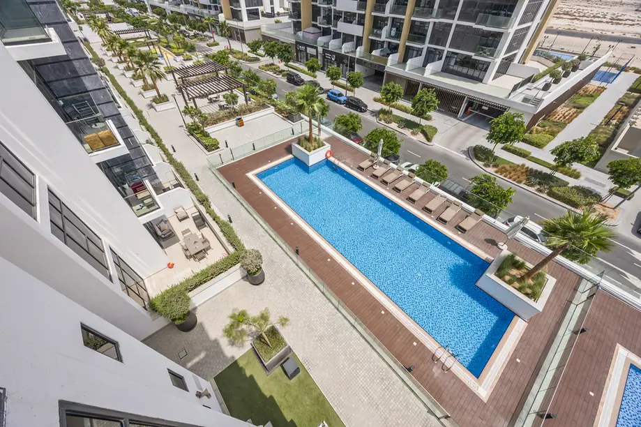 Aerial view of a modern residential complex with a rectangular blue swimming pool, lounge chairs, and palm trees surrounding the area.