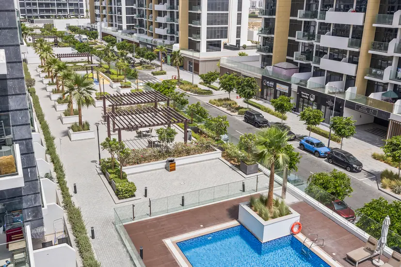 Aerial view of a modern apartment complex with a rectangular pool, palm trees, and landscaped courtyards along a tree-lined street.
