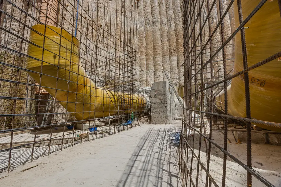 Underground construction site with a large yellow tunnel section wrapped in wire mesh and concrete walls nearby.