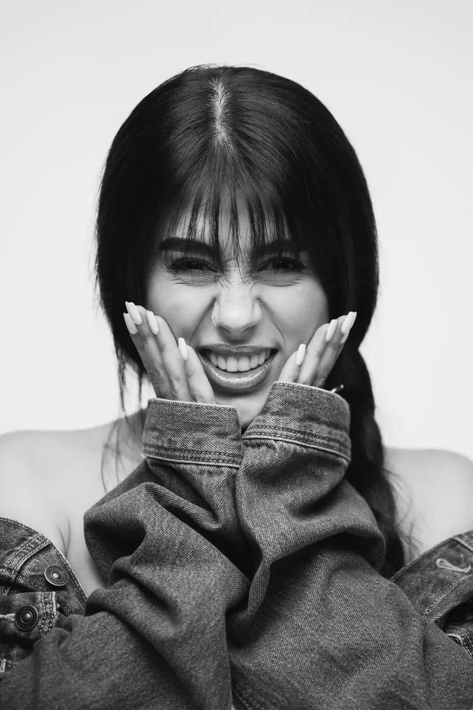 Young woman with long dark hair smiling, denim jacket sleeves pulled up to her face.