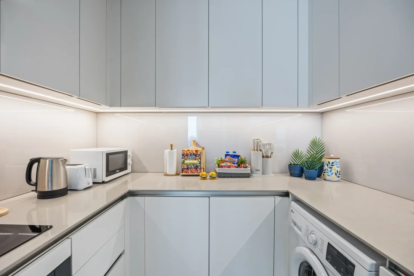 Modern minimalist kitchen with light gray cabinets, white countertops, and under-cabinet lighting.