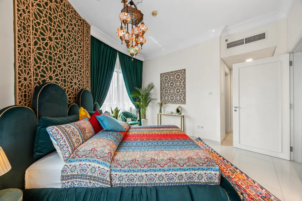 Luxurious bedroom with emerald velvet upholstered bed, colorful patterned bedding, and ornate wooden lattice screen on the left.