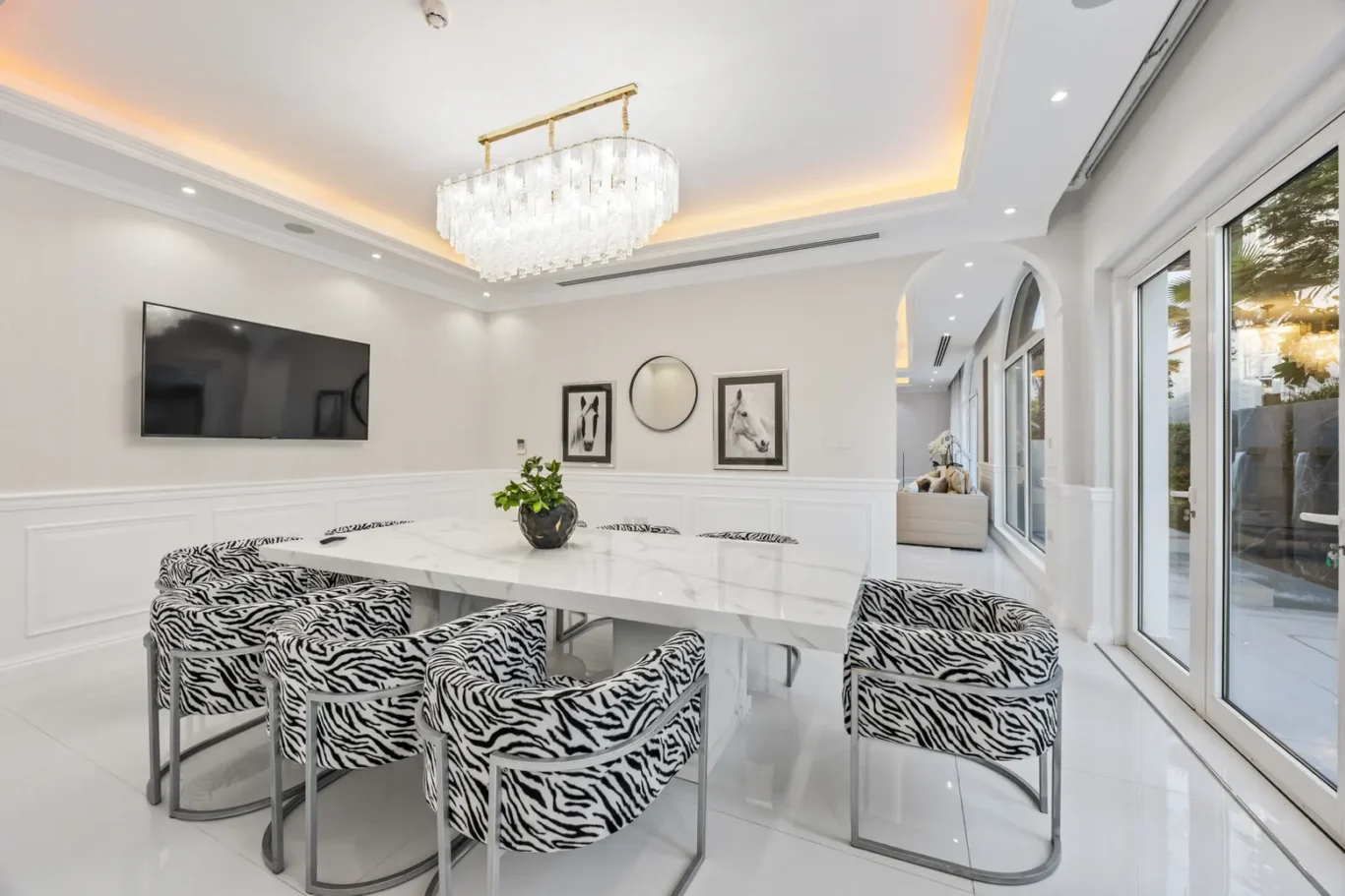 Bright contemporary dining room with a white marble table and zebra-patterned chairs around it, chandelier overhead, and glass doors nearby.