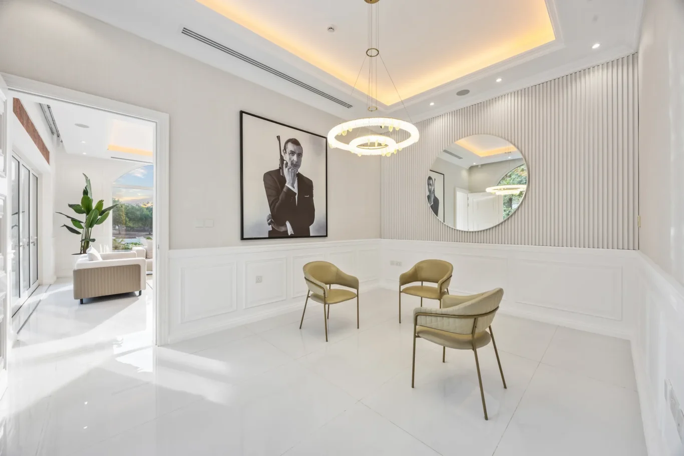 Modern white waiting room with a circular chandelier, beige chairs, and a black-and-white portrait of a man in a suit on the wall.