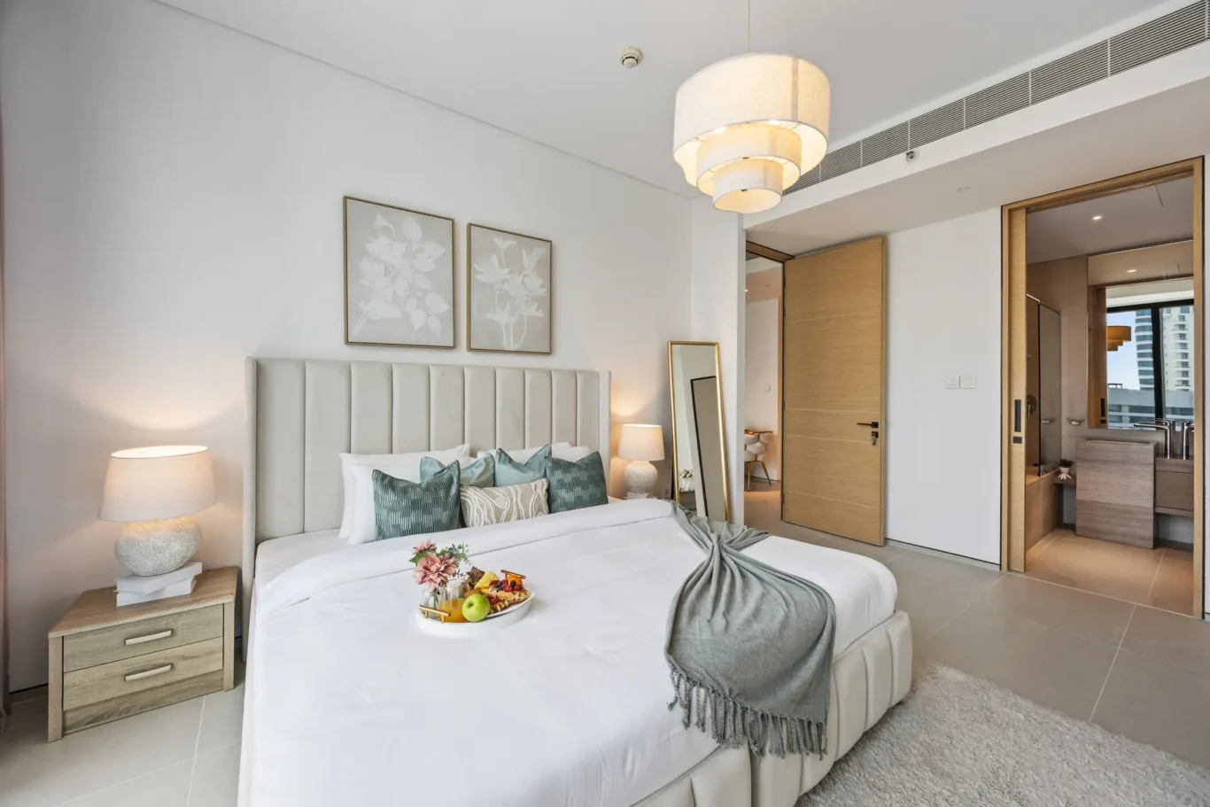 Hotel bedroom with a tall padded headboard, white bedding, teal cushions, and two bedside lamps on either side.