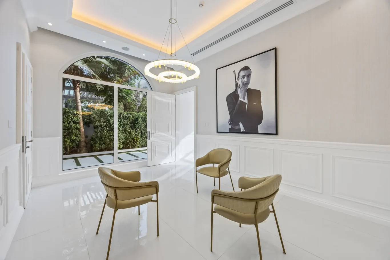 Modern white waiting area with arched glass door, circular pendant light, and four beige chairs around a large framed black-and-white portrait.