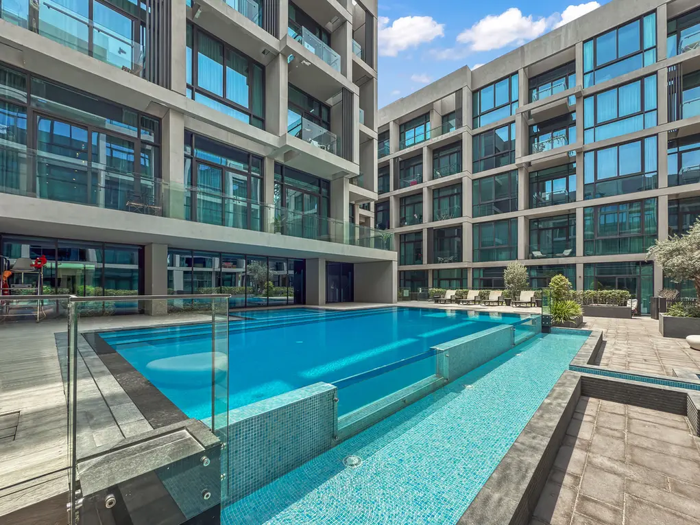 Modern residential complex with a rectangular outdoor pool and sun deck on a sunny day