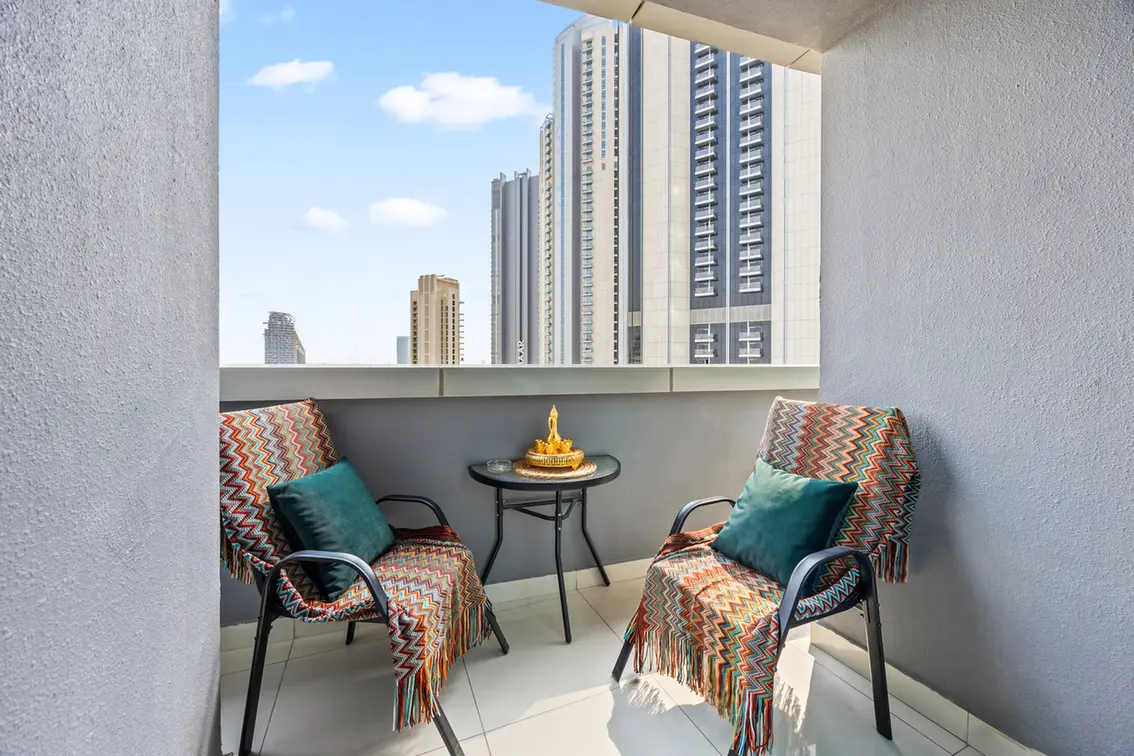 Balcony seating area with two patterned armchairs, teal cushions, a small round table, and a city skyline in the background.
