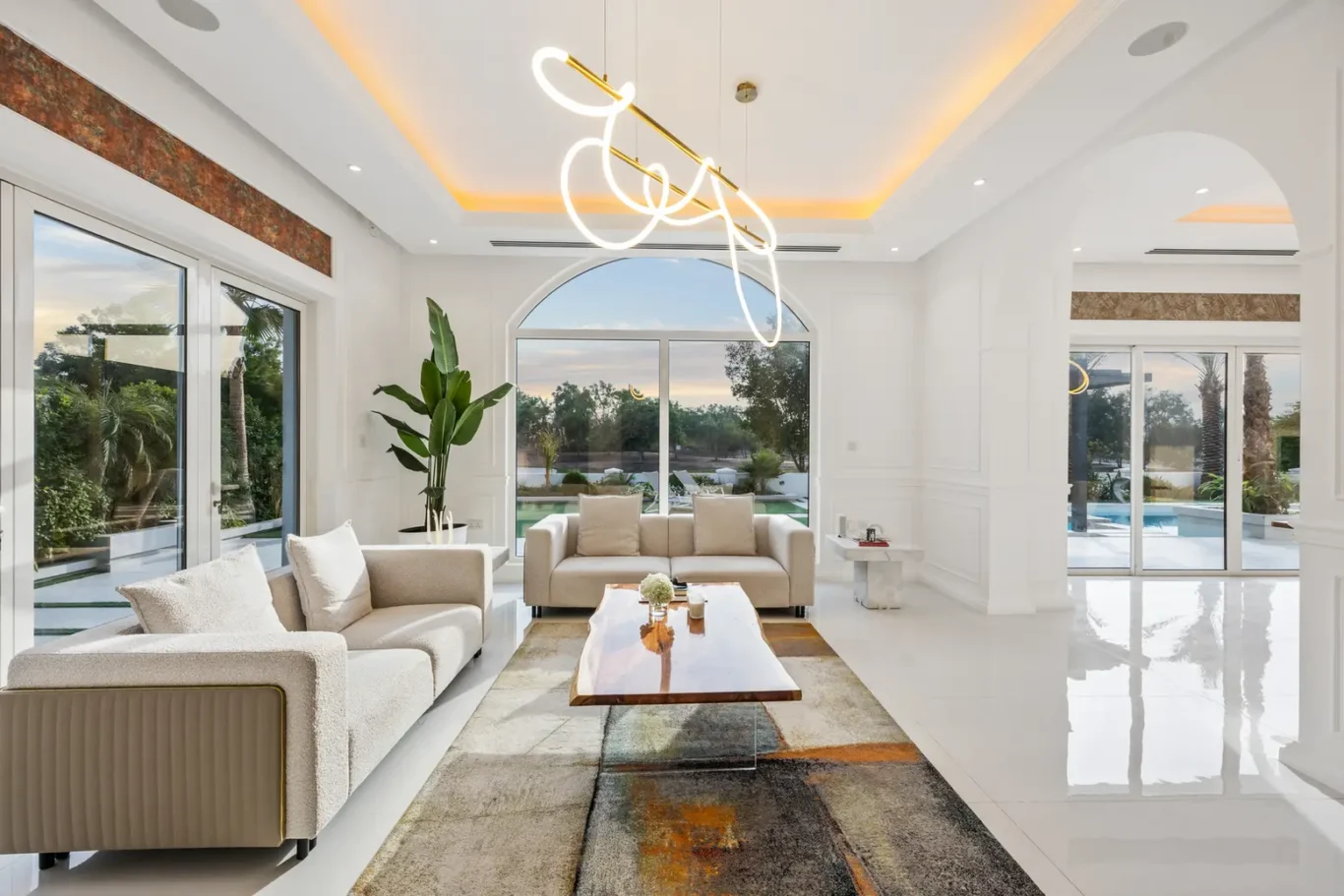 Bright modern living room with white furniture, an arched window, and a sculptural pendant chandelier outside daylight glare.