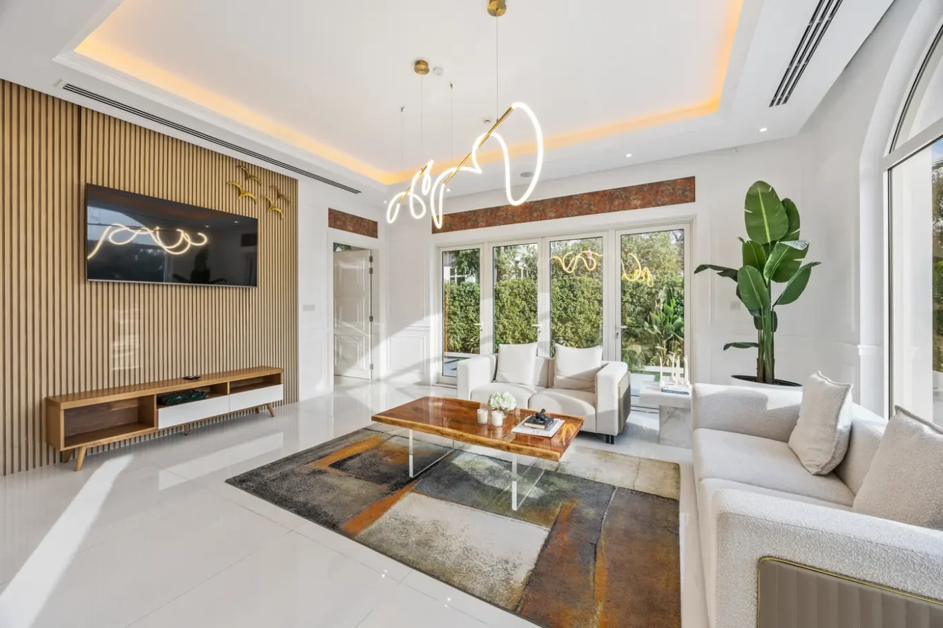 Bright modern living room with white furniture, a wooden slat wall, wall-mounted TV, and glass doors to the garden.