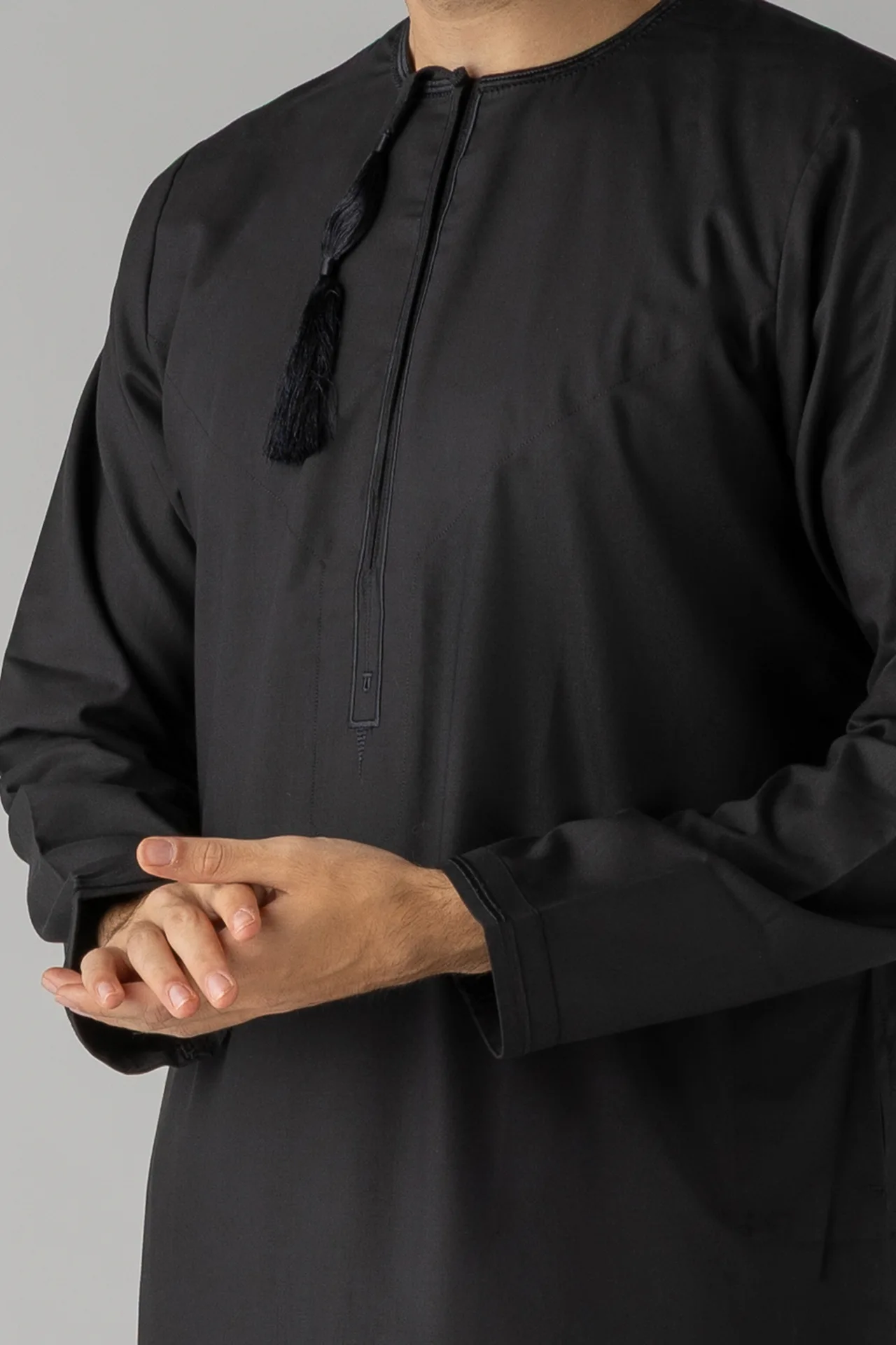 Man wearing a black traditional tunic with a black tassel necklace hanging from the collar, close-up of upper body.